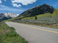 the road is paved with yellow markings and has a snowy mountain range in the background