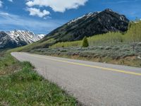 the road is paved with yellow markings and has a snowy mountain range in the background