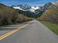 the road is paved with yellow markings and has a snowy mountain range in the background