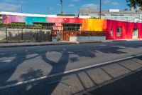 colorful building with tree shadow at the corner on the side of the road while cars are passing by