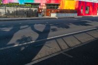 colorful building with tree shadow at the corner on the side of the road while cars are passing by