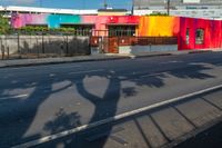 colorful building with tree shadow at the corner on the side of the road while cars are passing by