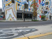 a city sidewalk with many different colored murals on it and there is a fire hydrant at the curb in front of the building