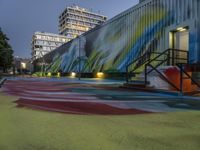 a colorful graffiti painted area next to a tall building at night with stairs and street lights