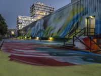 a colorful graffiti painted area next to a tall building at night with stairs and street lights