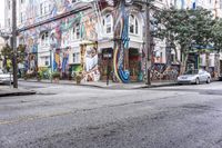 a city street with graffiti covering a colorful building and trees in front of it while parked cars sit nearby the stoplight