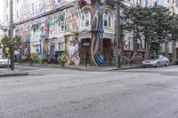 a city street with graffiti covering a colorful building and trees in front of it while parked cars sit nearby the stoplight