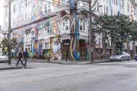 a city street with graffiti covering a colorful building and trees in front of it while parked cars sit nearby the stoplight
