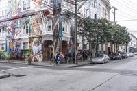 a city street with graffiti covering a colorful building and trees in front of it while parked cars sit nearby the stoplight