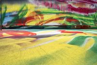 a colorful mural painted on the side of a building next to a sidewalk and two cars