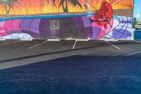 a colorful mural on a concrete wall is painted by someone holding a surfboard in the parking lot