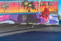 a colorful mural on a concrete wall is painted by someone holding a surfboard in the parking lot