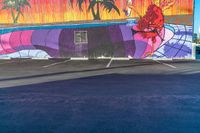 a colorful mural on a concrete wall is painted by someone holding a surfboard in the parking lot