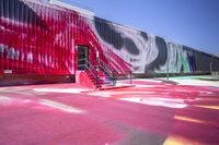 a parking lot that is painted with various colors of paint on it and a stair next to a red wall