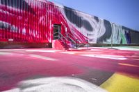 a parking lot that is painted with various colors of paint on it and a stair next to a red wall