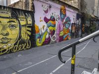 a colorful wall has been painted by various people on it's side, with two street railings