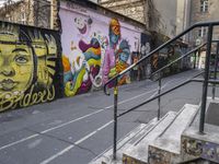 a colorful wall has been painted by various people on it's side, with two street railings