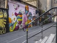 a colorful wall has been painted by various people on it's side, with two street railings