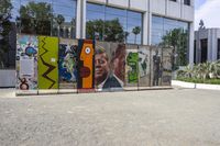 two colorful pieces of street art with building in background and trees reflected in glass window