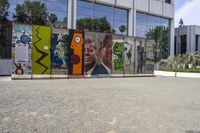 two colorful pieces of street art with building in background and trees reflected in glass window