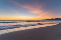 a colorful sunset at the beach with waves rolling in towards the shore and a plane flying through