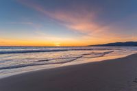 a colorful sunset at the beach with waves rolling in towards the shore and a plane flying through