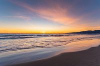 a colorful sunset at the beach with waves rolling in towards the shore and a plane flying through