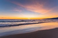 a colorful sunset at the beach with waves rolling in towards the shore and a plane flying through