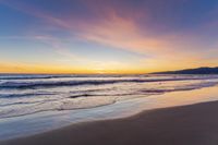 a colorful sunset at the beach with waves rolling in towards the shore and a plane flying through