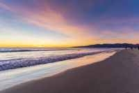 a colorful sunset at the beach with waves rolling in towards the shore and a plane flying through