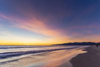 a colorful sunset at the beach with waves rolling in towards the shore and a plane flying through