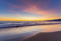 a colorful sunset at the beach with waves rolling in towards the shore and a plane flying through