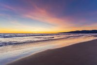 a colorful sunset at the beach with waves rolling in towards the shore and a plane flying through