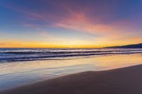 a colorful sunset at the beach with waves rolling in towards the shore and a plane flying through