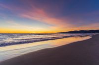 a colorful sunset at the beach with waves rolling in towards the shore and a plane flying through