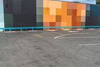 a building painted with a colorful wall and sidewalk in front of it, with cars parked on the street below