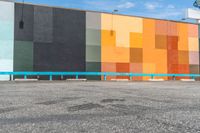 a building painted with a colorful wall and sidewalk in front of it, with cars parked on the street below