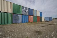 containers are lined up and stacked in a large field in a city area with some dirt