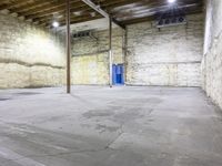 large empty concrete room with exposed ceiling and beams, showing fire hydrant outside, exposed wall behind