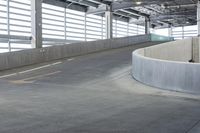 an empty parking area with concrete barriers and large windows in the wall above it,