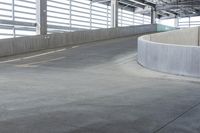 an empty parking area with concrete barriers and large windows in the wall above it,