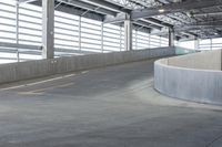 an empty parking area with concrete barriers and large windows in the wall above it,