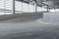 an empty parking area with concrete barriers and large windows in the wall above it,