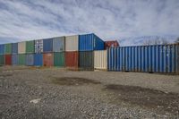 a group of cargo containers that are on the ground in a gravel field at a yard