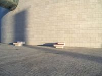 two concrete benches near a wall in an empty spot with blue sky behind them on a cobblestone street