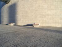 two concrete benches near a wall in an empty spot with blue sky behind them on a cobblestone street