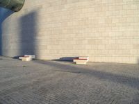 two concrete benches near a wall in an empty spot with blue sky behind them on a cobblestone street