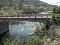 a view from a bridge overlooking trees and a mountain range of hills behind a bridge