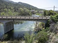 a view from a bridge overlooking trees and a mountain range of hills behind a bridge