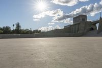 a concrete bridge spanning the width of a skateboard park and ramps under the sun and clouds